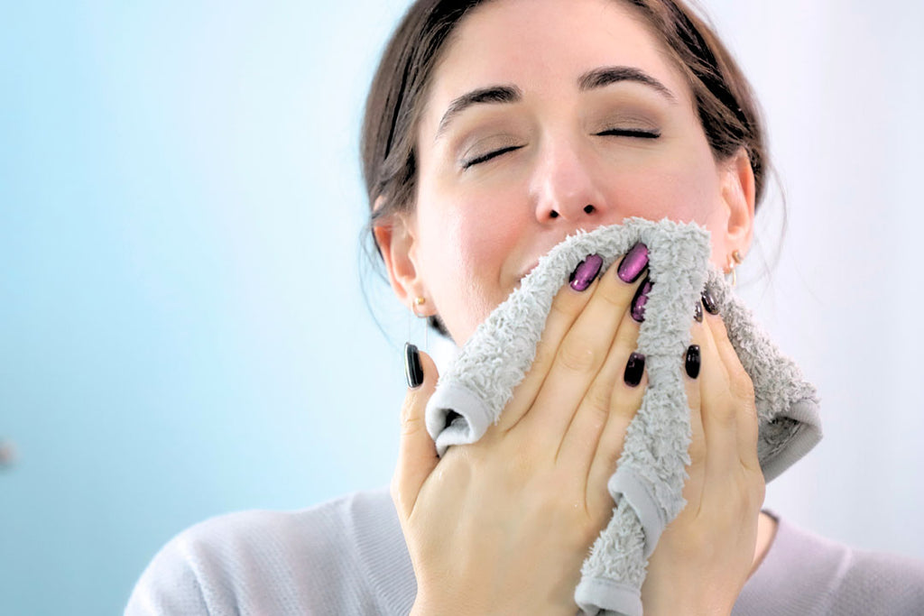 woman using a grey face cloth to wipe her face