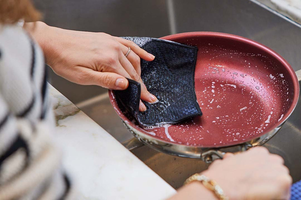 hand scrubbing a pan with reusable scrub cloth